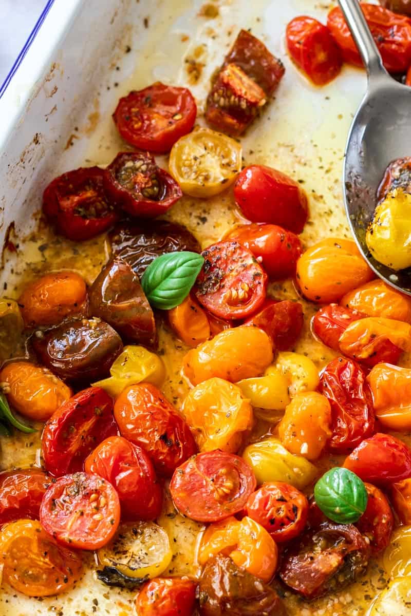 Baking dish with Roasted Cherry Tomatoes, with a silver spoon scooping into them.