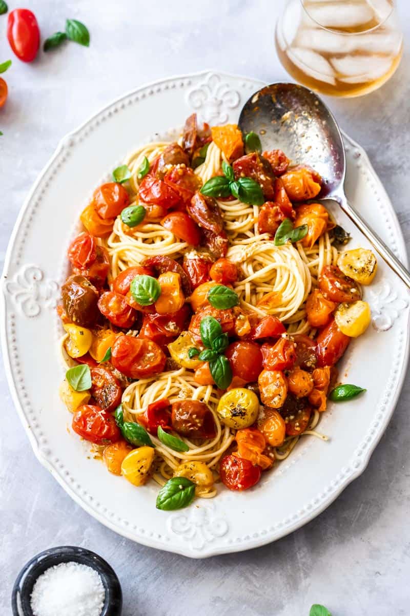 White oval plate topped with Roasted Cherry Tomato Pasta, with a silver spoon on the side.