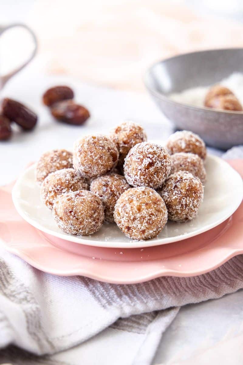 Salted Caramel Bliss Balls, sitting on a white plate on top of a pink plate and tea towel.