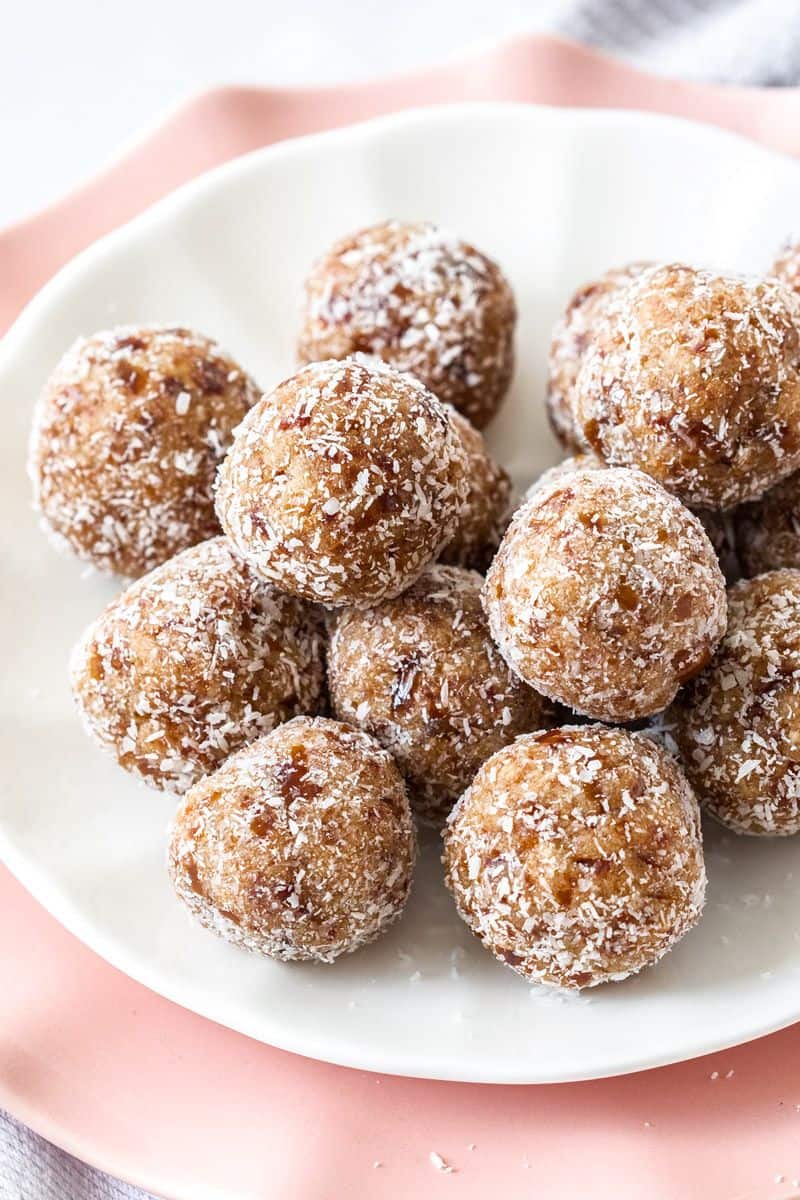 Salted Caramel Bliss Balls, sitting on a white plate on top of a pink plate and tea towel.