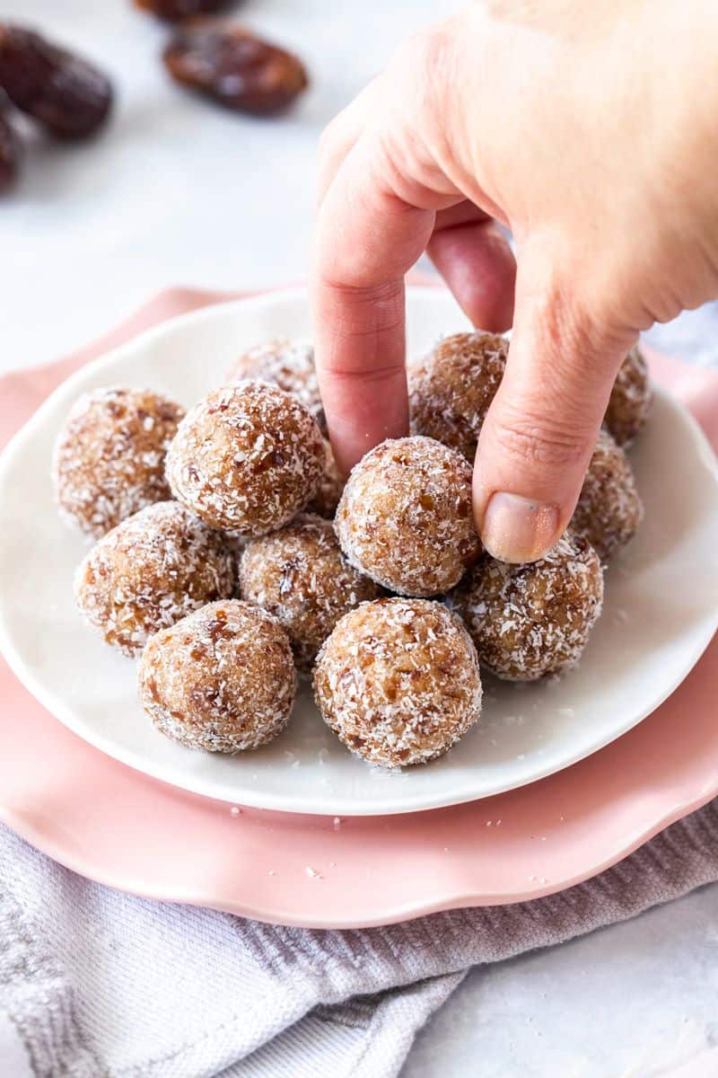 Hand reaching to pick up a Bliss Ball from a white plate on top of a pink plate.