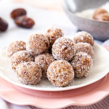 Salted Caramel Bliss Balls, sitting on a white plate on top of a pink plate and tea towel.