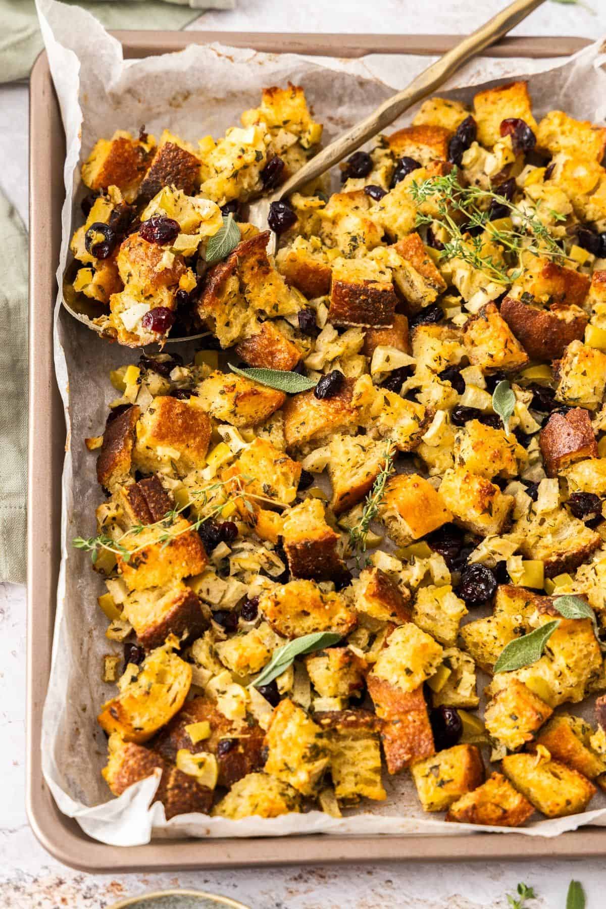 Crispy Sheet Pan Stuffing, sitting on a bench top with a gold spoon scooping some up.