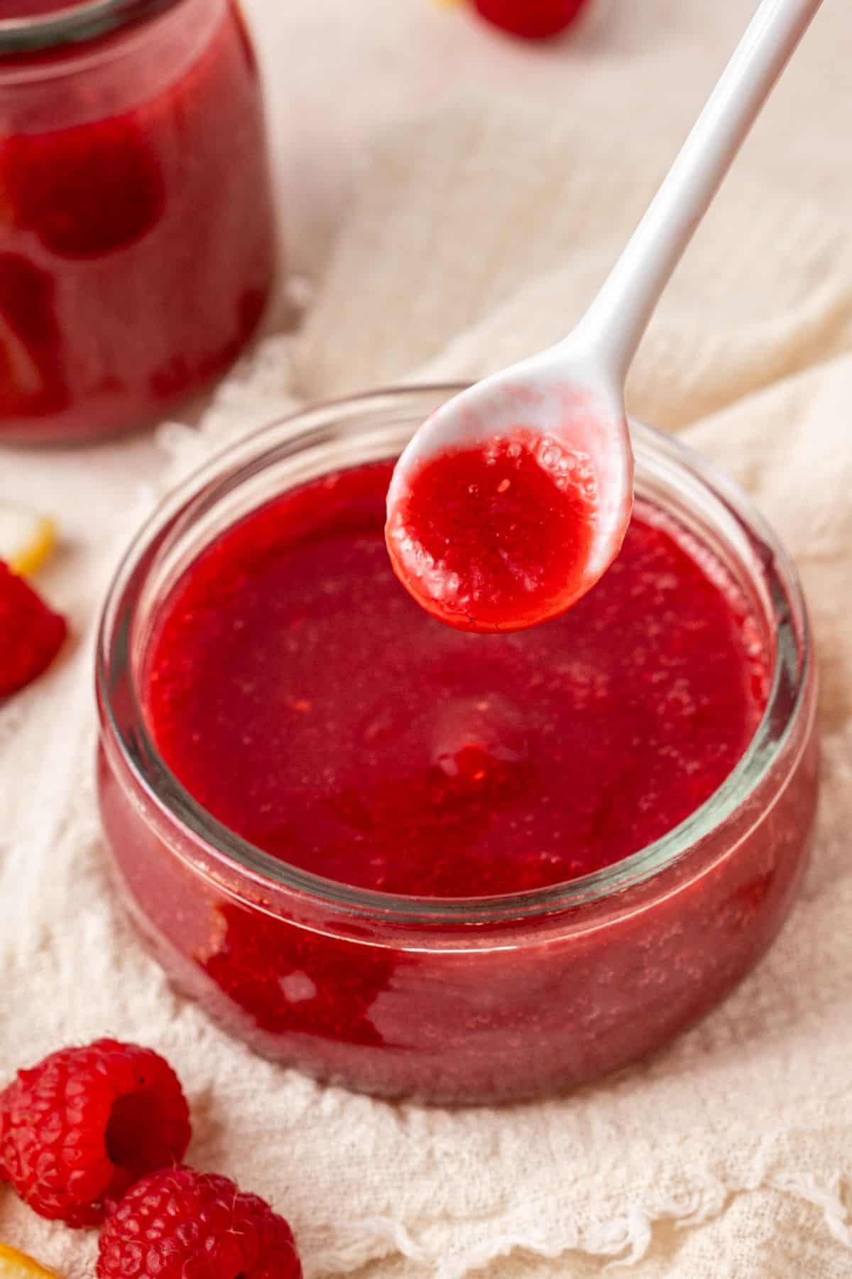 Round glass dish of Raspberry Sauce, with a spoon lifting out a small amount.