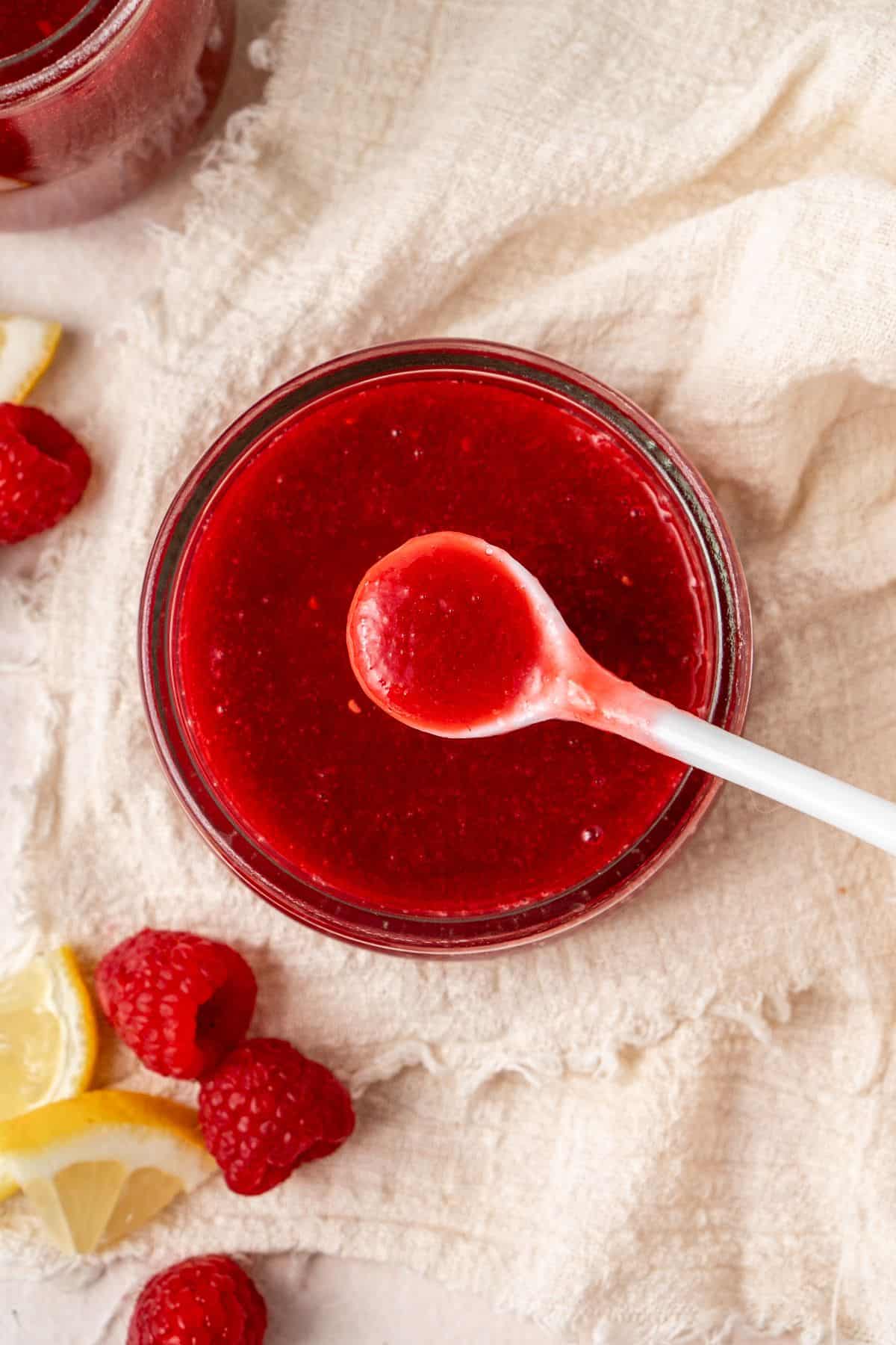 Round glass dish of Raspberry Sauce, with a spoon lifting out a small amount.