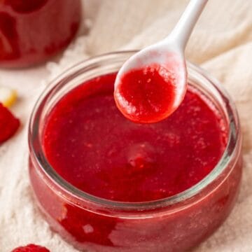 Round glass dish of Raspberry Sauce, with a spoon lifting out a small amount.