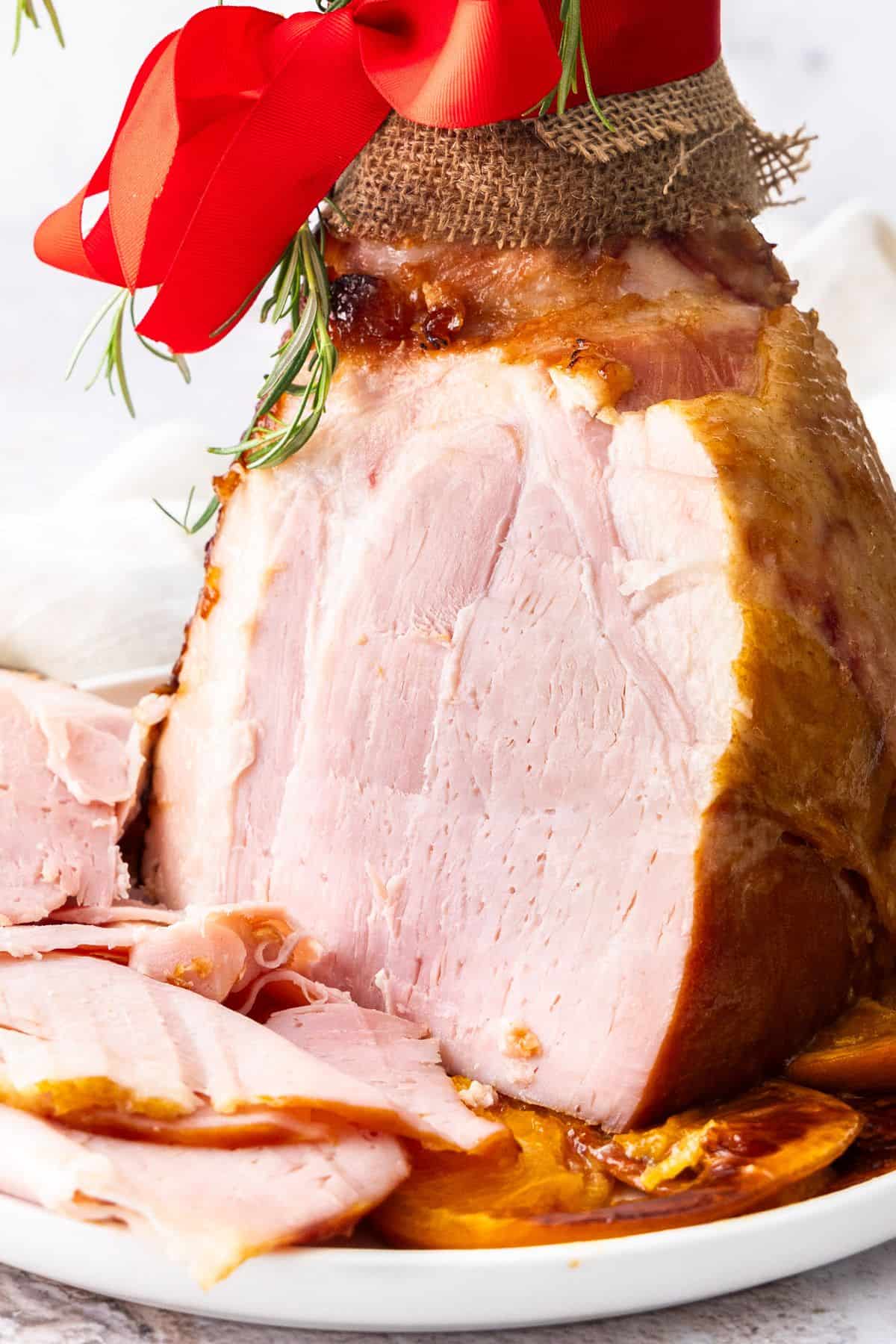 Maple Glazed Ham, sitting on a round white plate, with some slices having been carved.