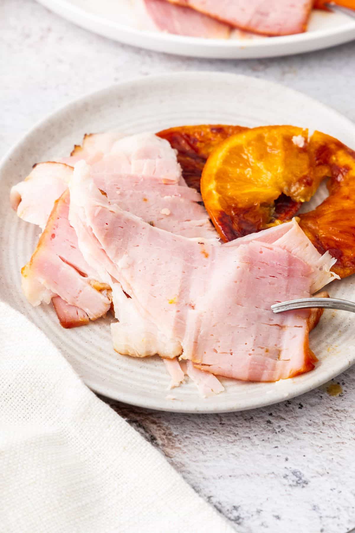 Slices of carved ham on a round white plate, with a couple of slices of orange on the edge.