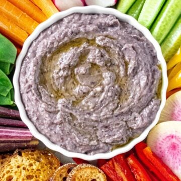 Dip platter of Black Bean Dip surrounded by various cut vegetables and some toasts.