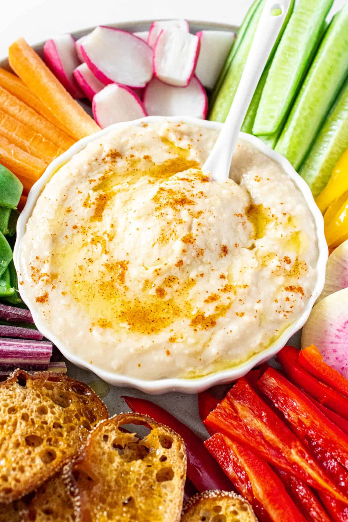 Dip platter featuring Cannellini Bean Dip and a selection of sliced vegetables and some toasts.