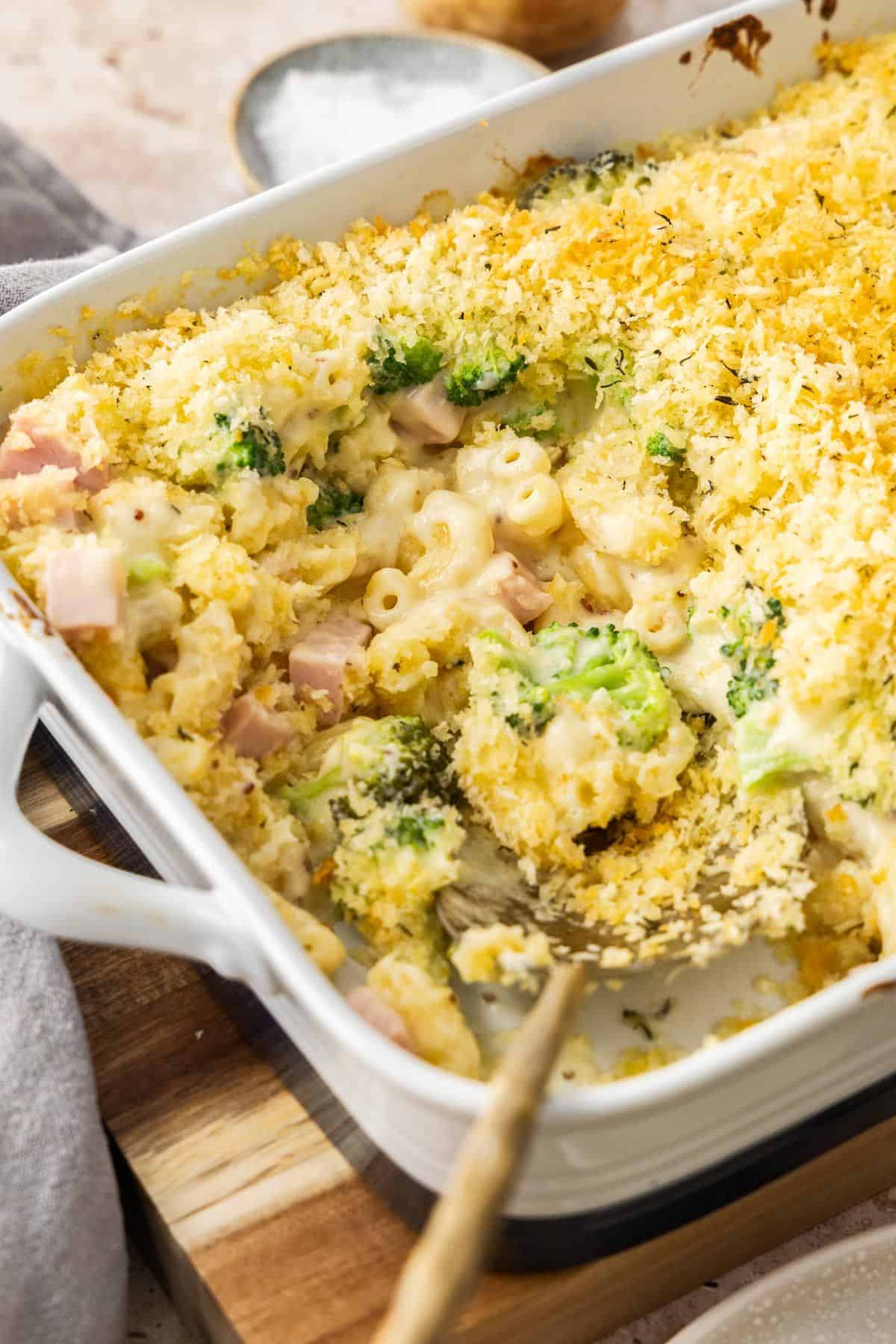 White rectangular dish of Creamy Ham Pasta Bake, sitting on a wooden board with a serve having been removed.