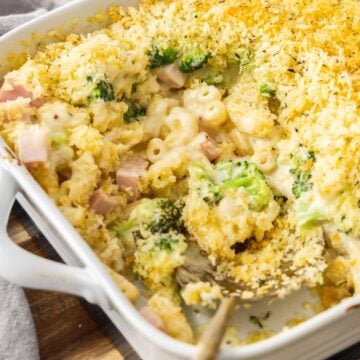 White rectangular dish of Creamy Ham Pasta Bake, sitting on a wooden board with a serve having been removed.