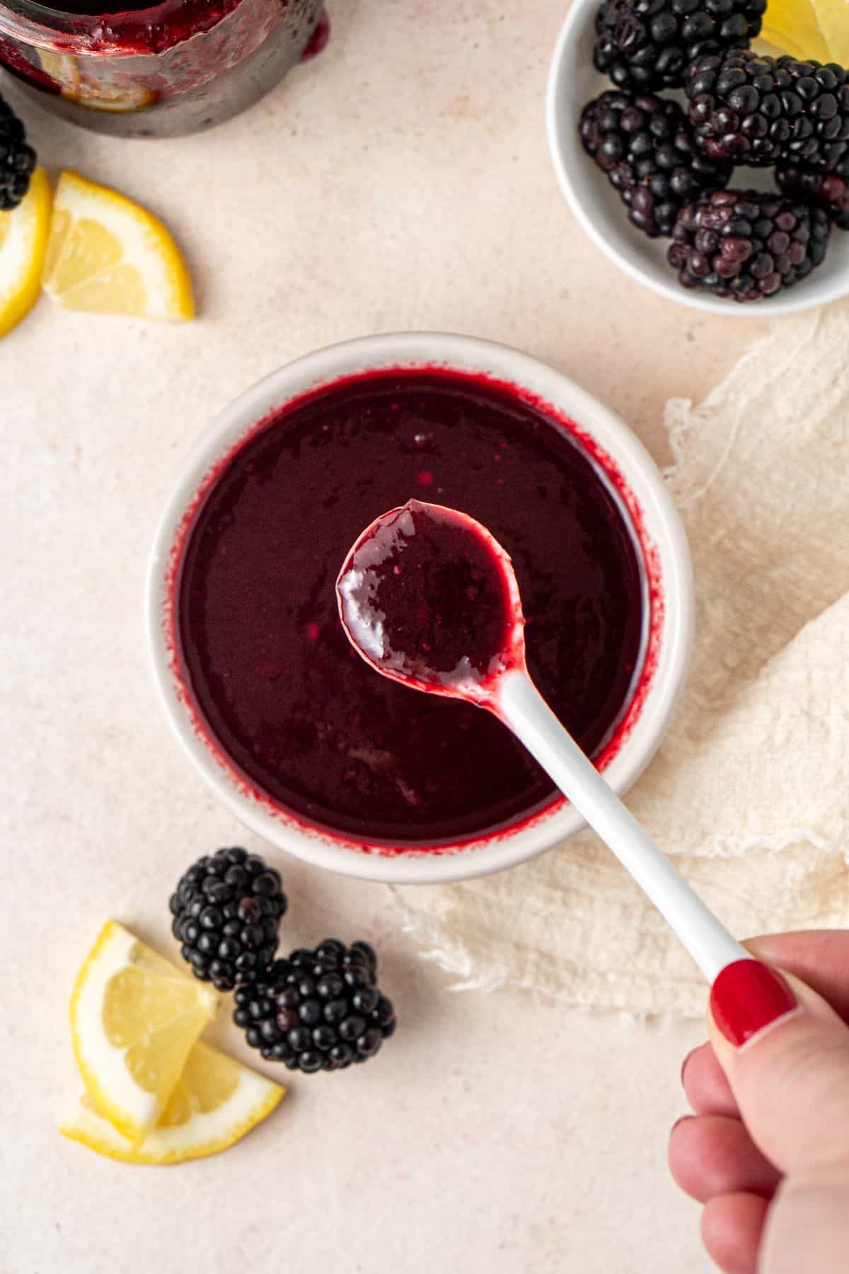 Small white dish of Blackberry Sauce, with a white spoon dipping into it.