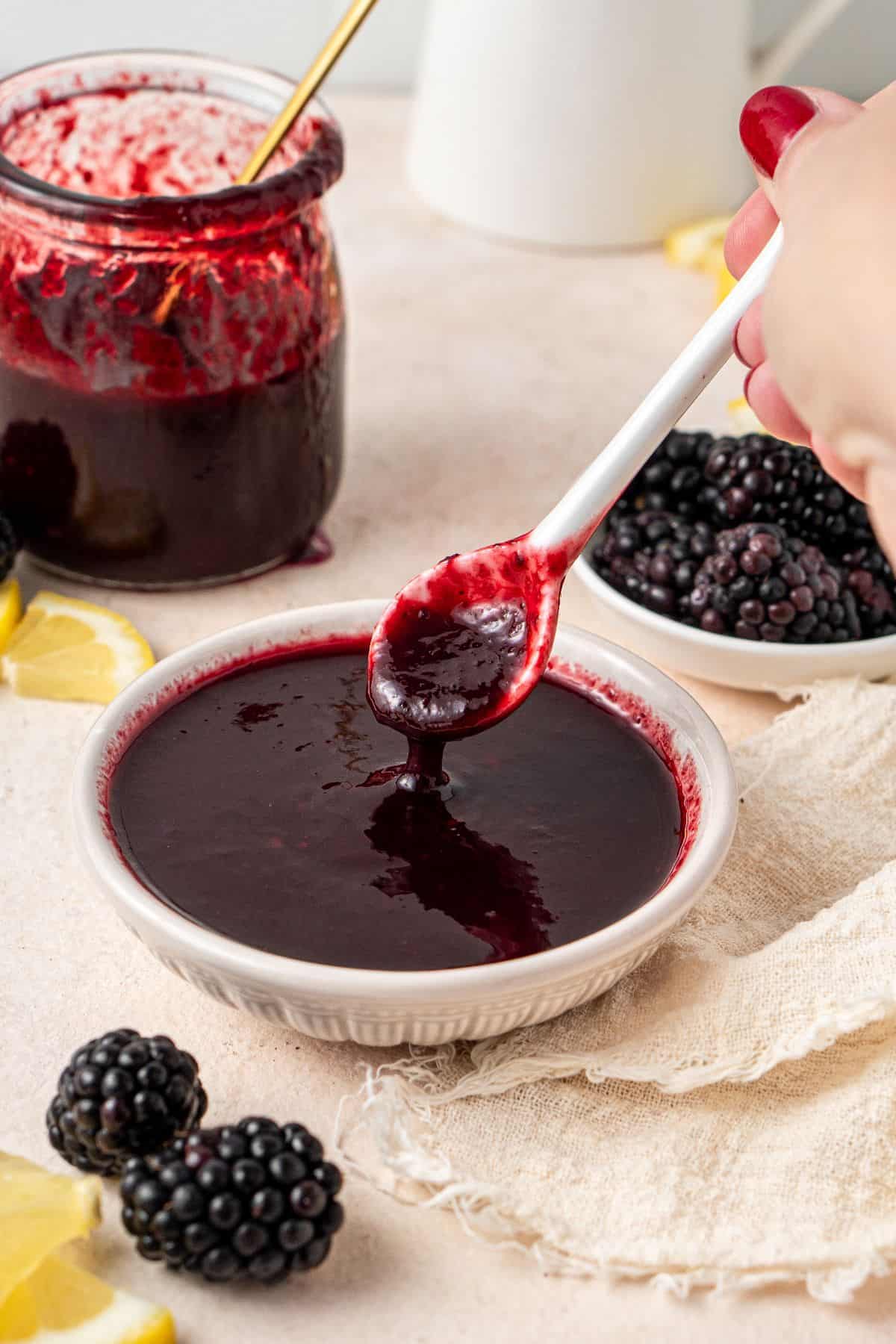 Small white dish of Blackberry Sauce, with a white spoon dipping into it.