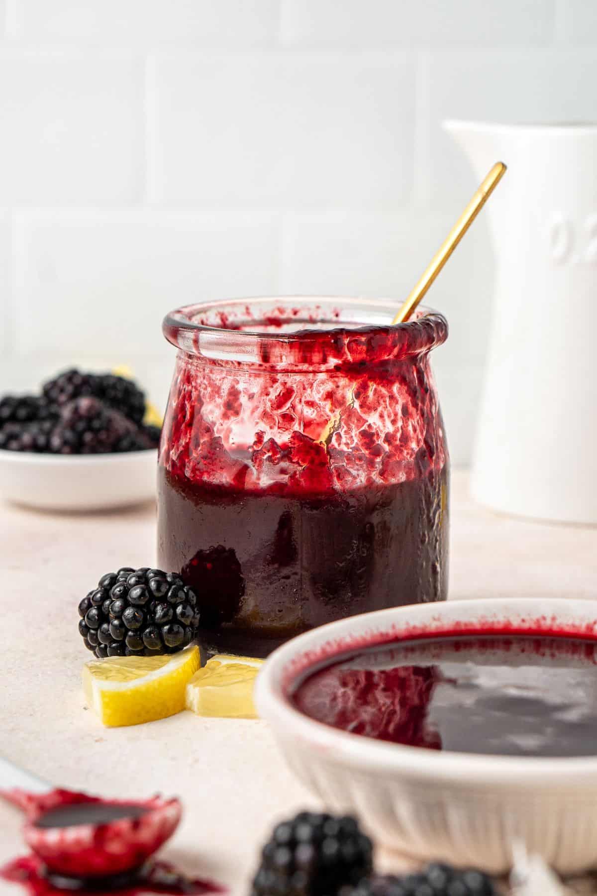 Jar of Blackberry Sauce, with a gold spoon resting in it.