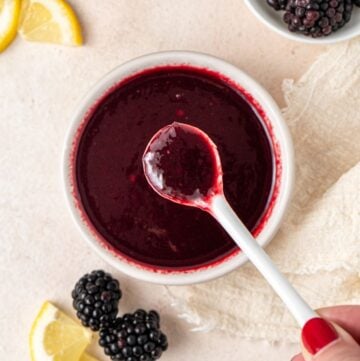 Small white dish of Blackberry Sauce, with a white spoon dipping into it.