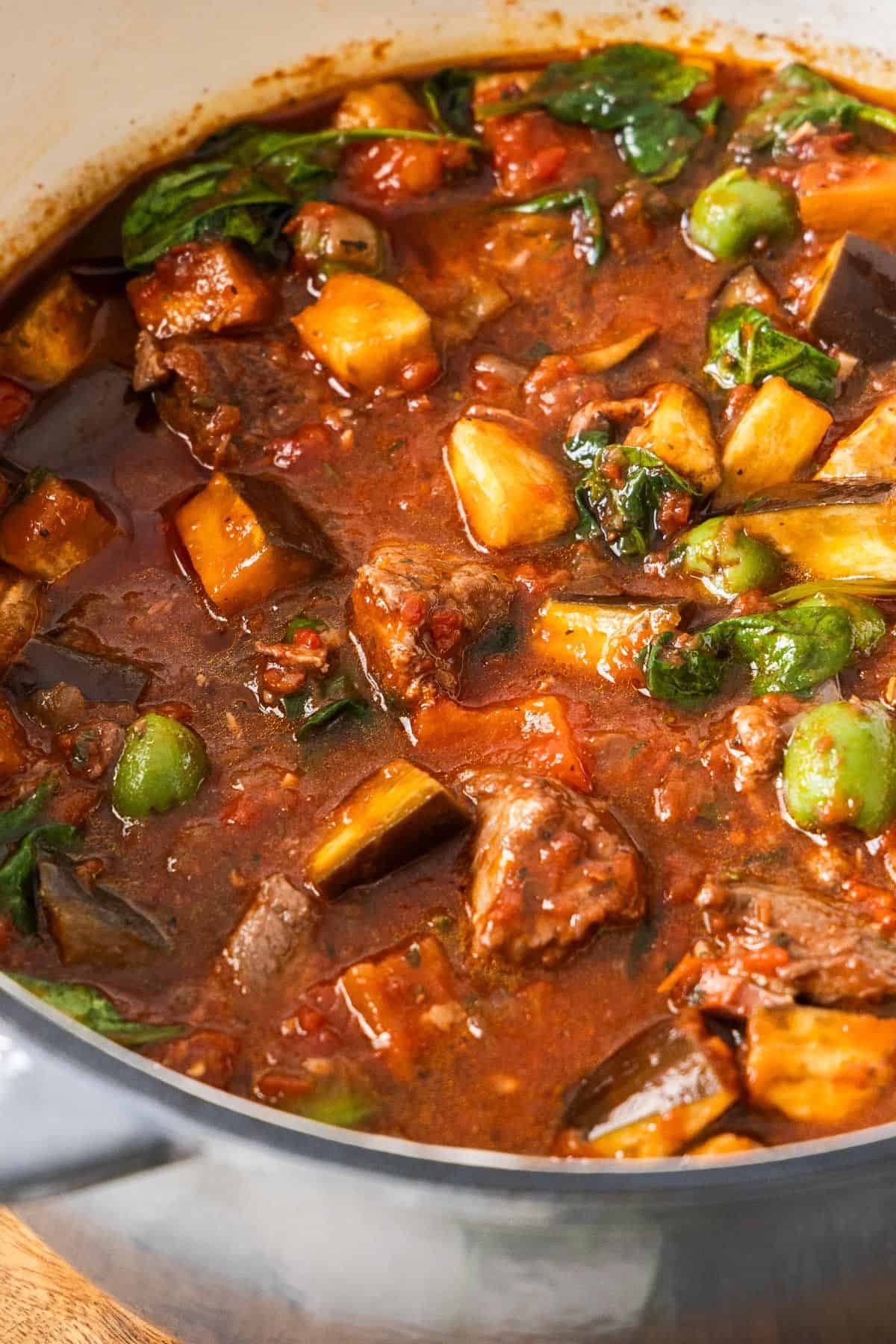 Mediterranean Lamb Stew, in a large grey saucepan sitting on a wooden board.