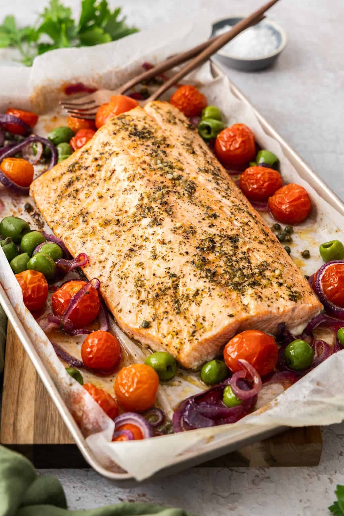 Sheet pan with side of Mediterranean Salmon and vegetables around the edge, with serving utensils.