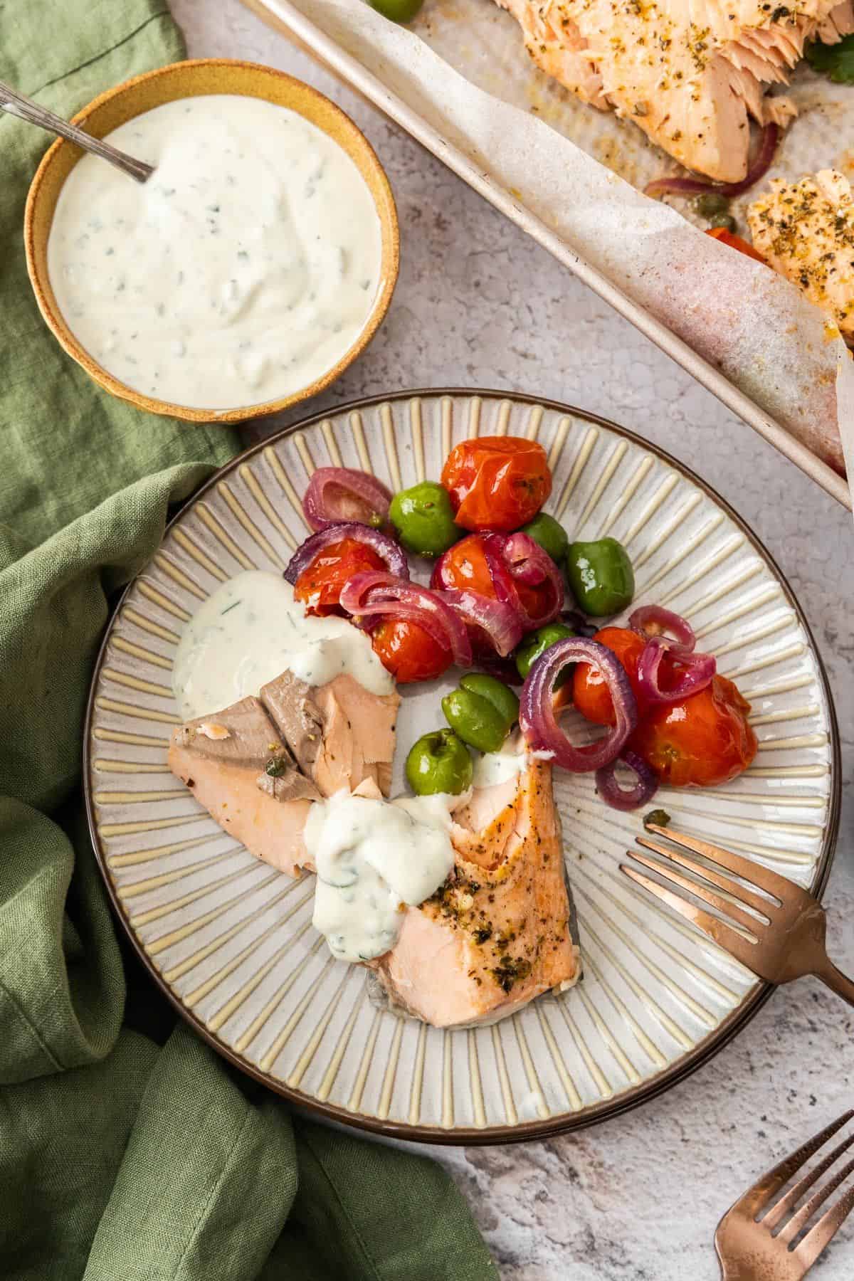 Round plate with serve of Mediterranean Salmon and vegetables, drizzled with yoghurt sauce, with a fork on the edge.