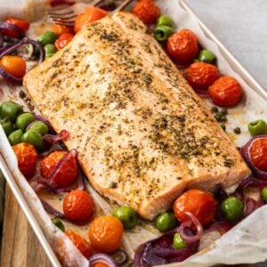 Sheet pan with side of Mediterranean Salmon and vegetables around the edge, with serving utensils.