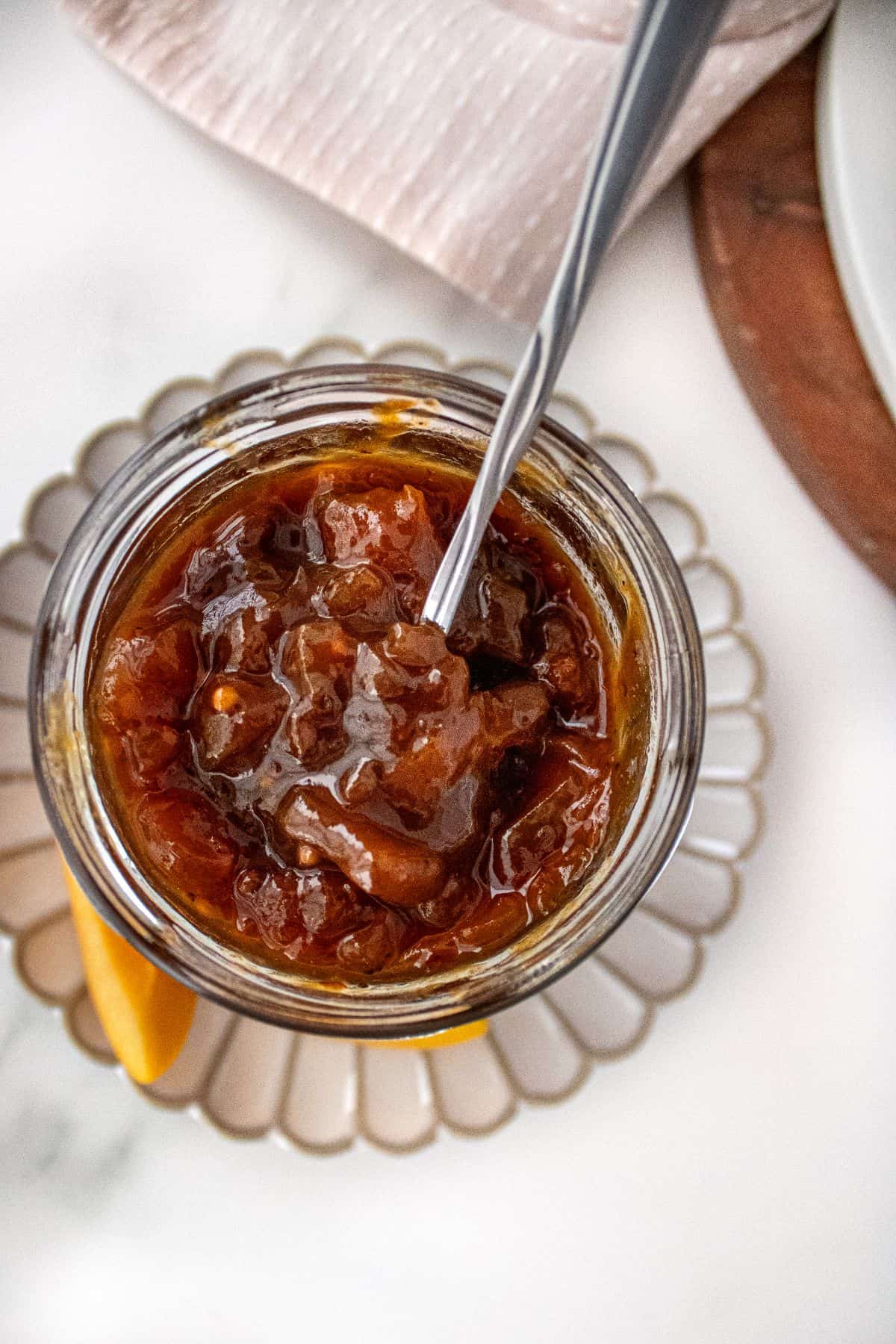 Open jar of Apricot Chutney on a small white plate, with a spoon sitting in the jar.