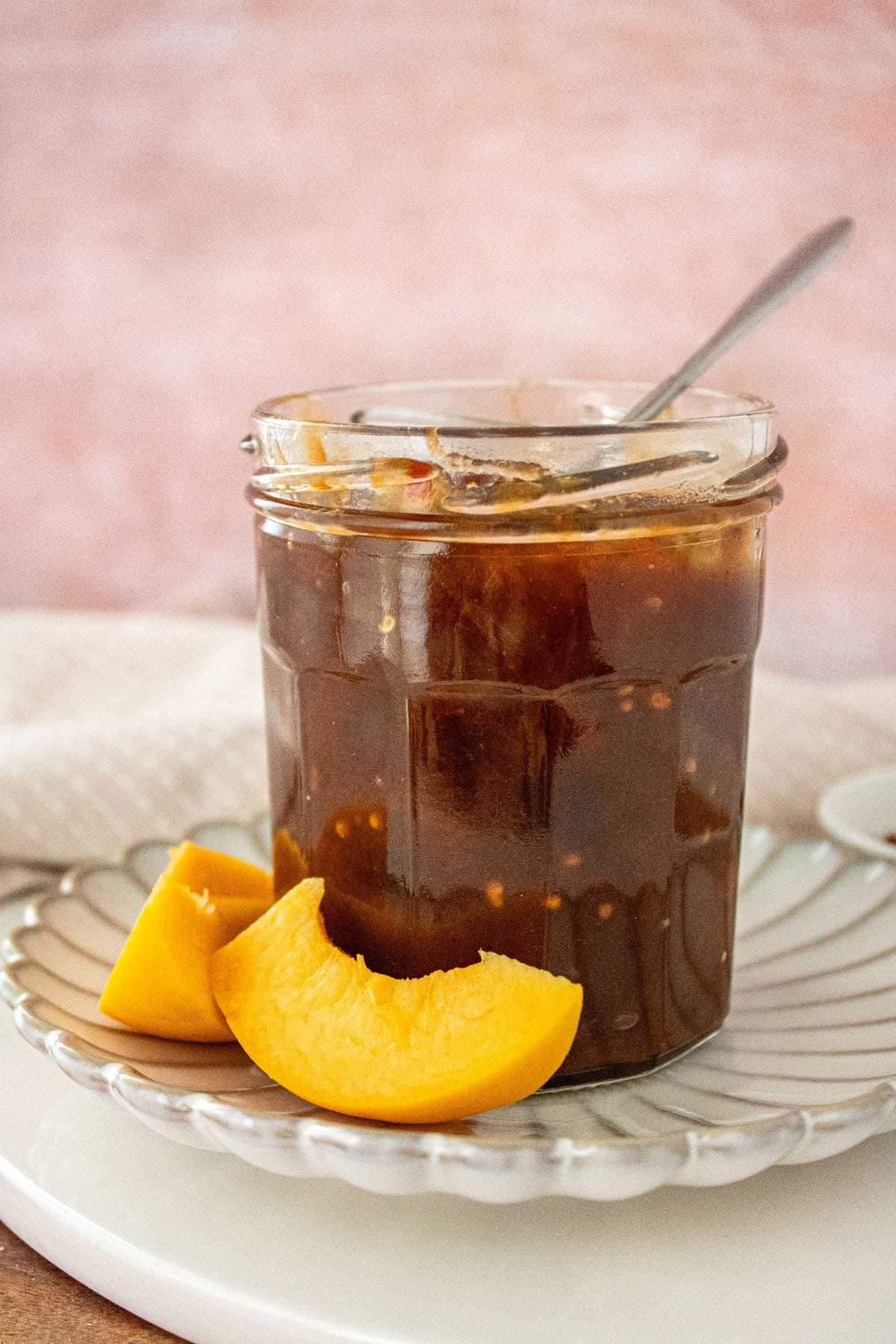 Open jar of Apricot Chutney on a small white plate, with a spoon and some apricot pieces around the edge.