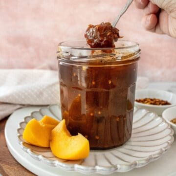 Open jar of Apricot Chutney on a small white plate, with a spoon scooping up some chutney.