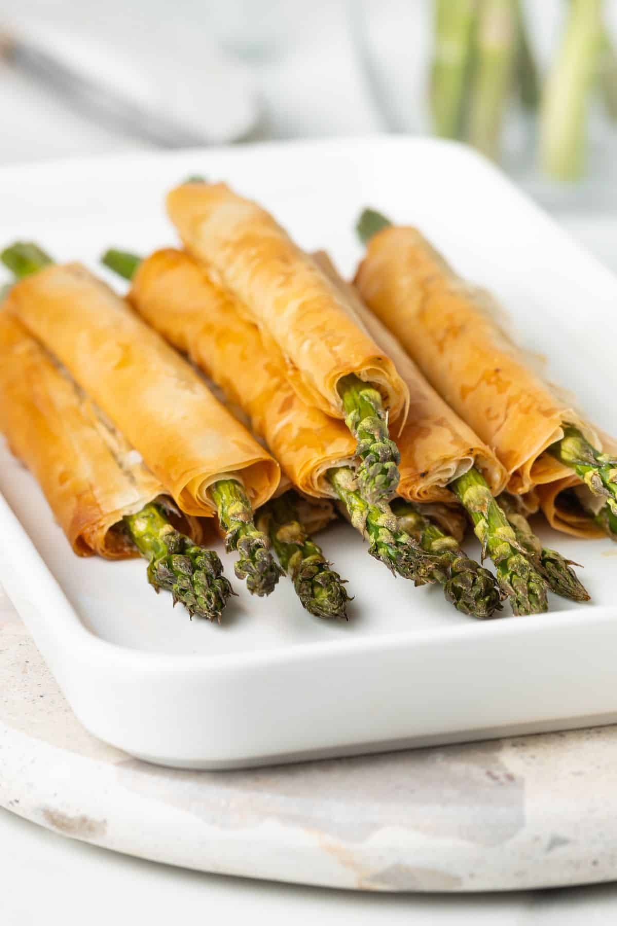 White Platter of Asparagus Filo Rolls, sitting on a marble board.