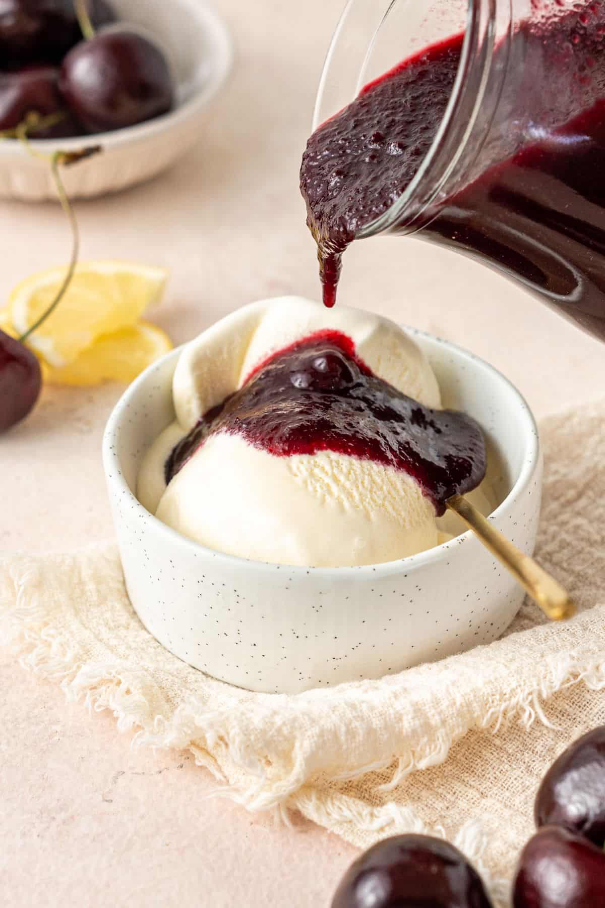 Jug of Cherry Sauce pouring some sauce over a small bowl of vanilla ice cream.