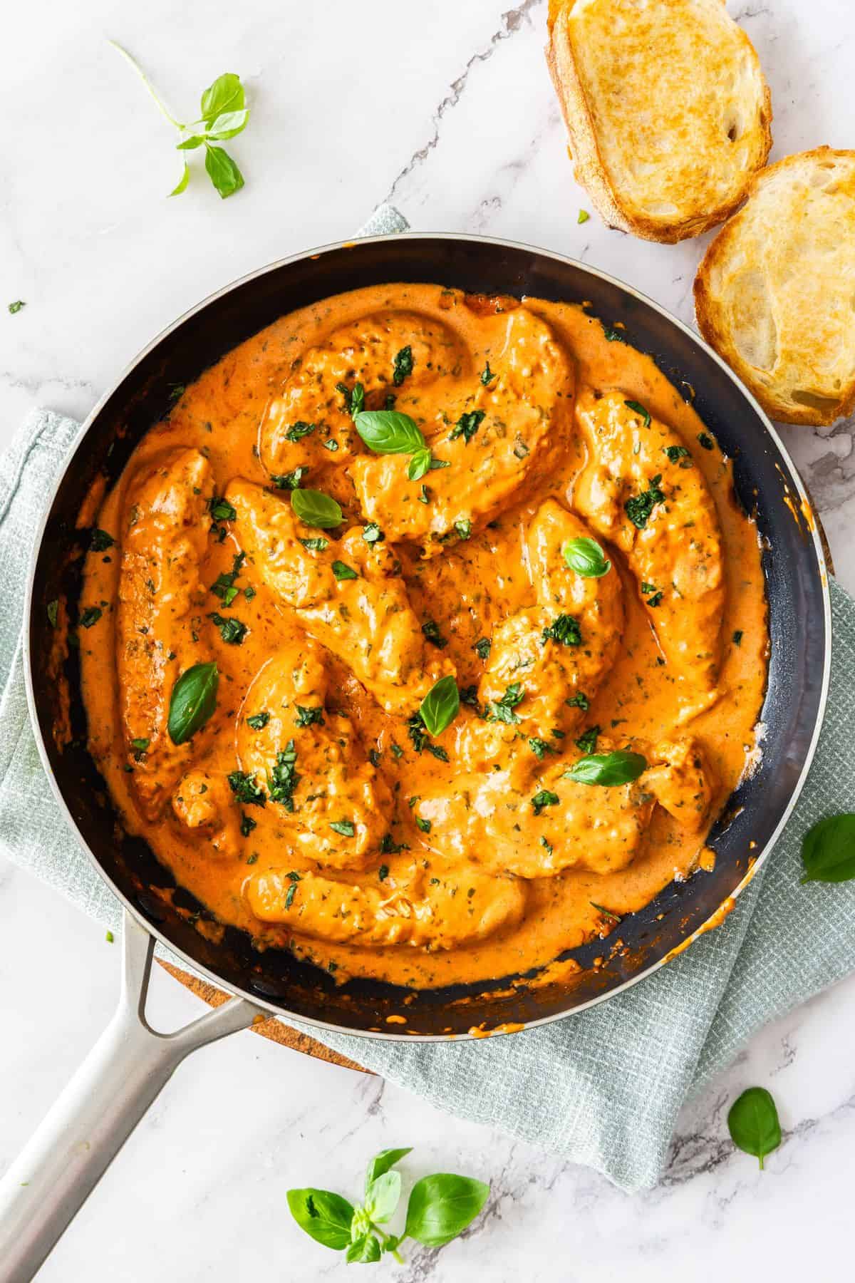 Frying pan with Creamy Tomato Chicken, garnished with some fresh basil, sitting on a pale green cloth.