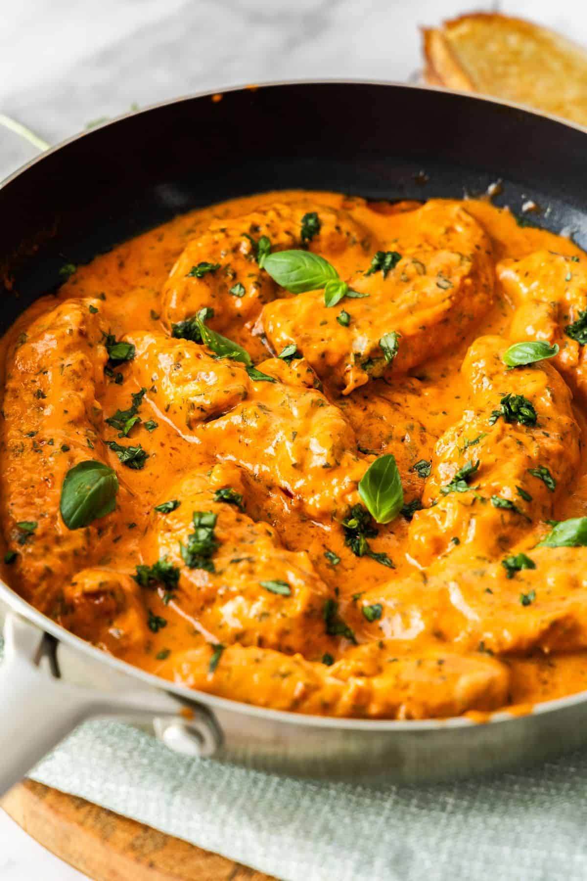Frying pan with Creamy Tomato Chicken, garnished with some fresh basil, sitting on a pale green cloth.