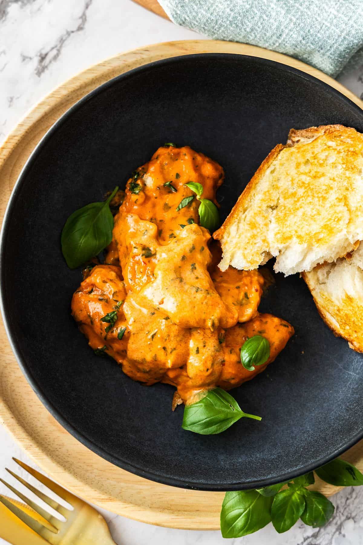 Serve of Creamy Tomato Chicken on a round black plate, with some toasted bread on the edge.