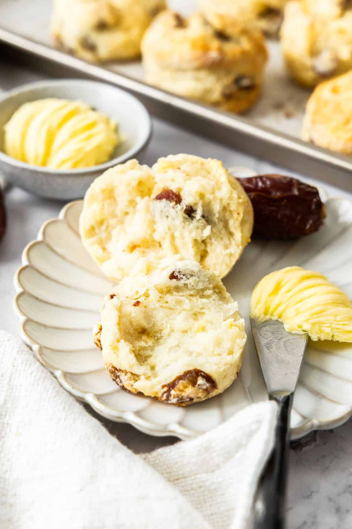 Round plate with a Date and Lemon Scone cut in half, with a knife and some butter on the edge.
