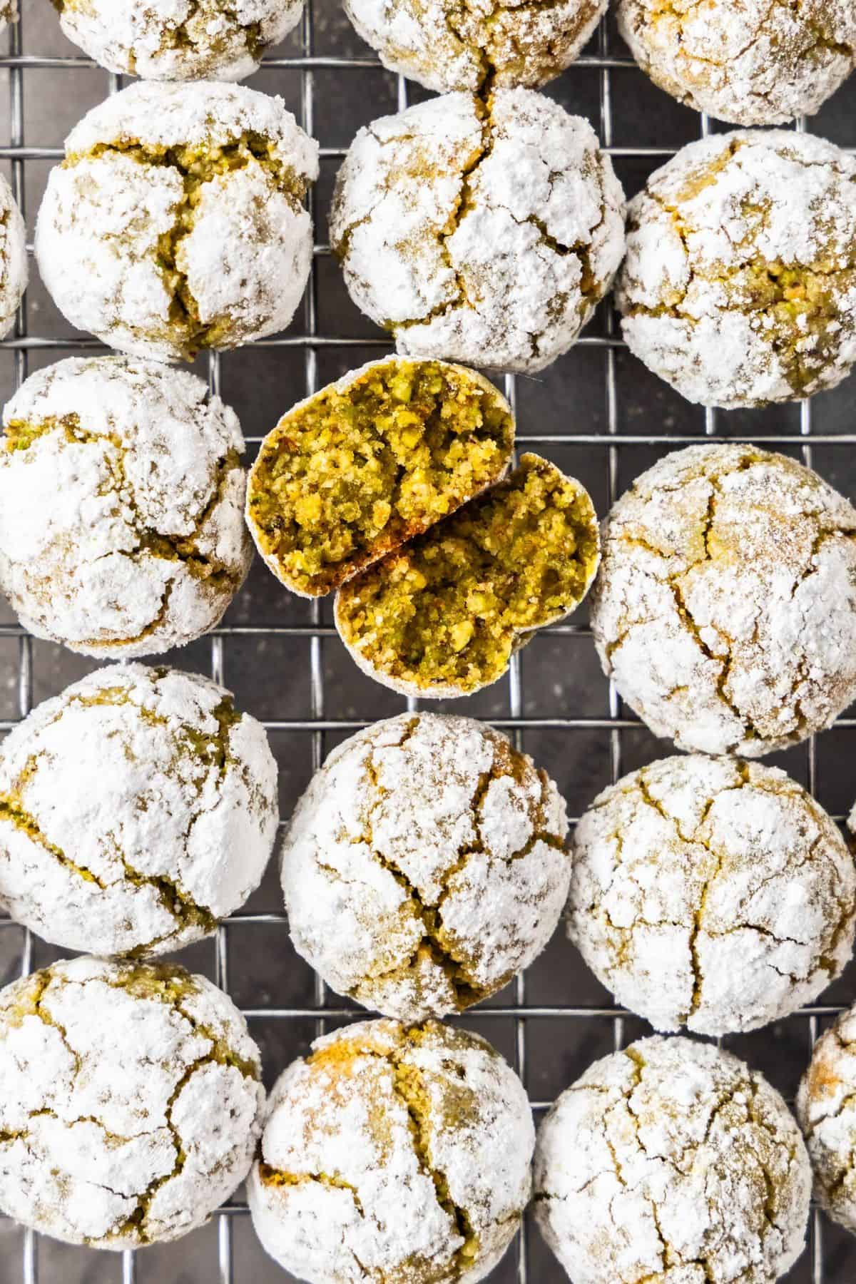 Cooling rack topped with freshly baked Gluten-Free Pistachio Cookies, one broken in half to show the interior.