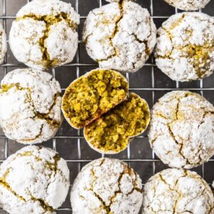 Cooling rack topped with freshly baked Gluten-Free Pistachio Cookies, one broken in half to show the interior.