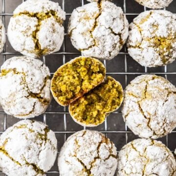 Cooling rack topped with freshly baked Gluten-Free Pistachio Cookies, one broken in half to show the interior.