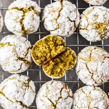 Cooling rack topped with freshly baked Gluten-Free Pistachio Cookies, one broken in half to show the interior.