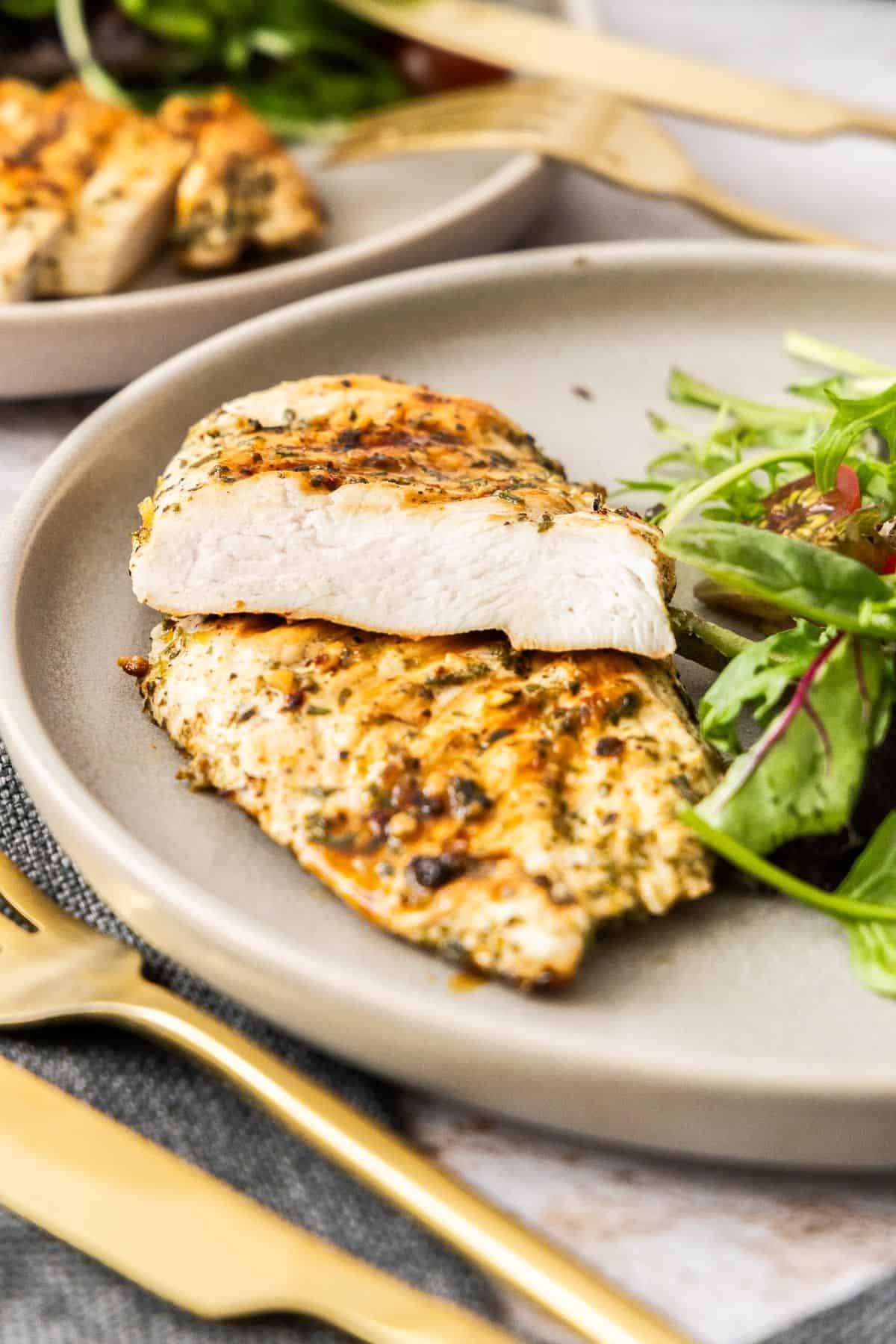 Round grey plate with one Marinated Chicken Breast, cut in half, to show the tender flesh, with a side salad.