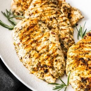 White oval platter of Marinated Chicken Breast on a grey cloth, plate garnished with some rosemary.