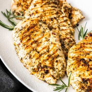 White oval platter of Marinated Chicken Breast on a grey cloth, plate garnished with some rosemary.
