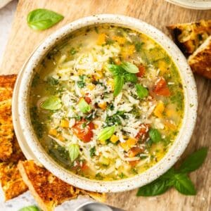 Bowl of Mediterranean Orzo Soup, garnished with Parmesan and Basil, with some toasted bread on the edge.
