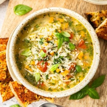 Bowl of Mediterranean Orzo Soup, garnished with Parmesan and Basil, with some toasted bread on the edge.