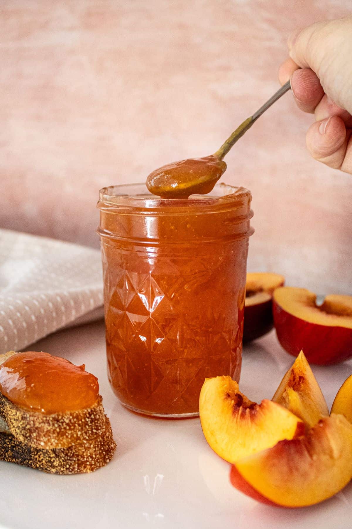 Open jar of Nectarine Jam with a spoon scooping up some jam, and some nectarine pieces around the edge.