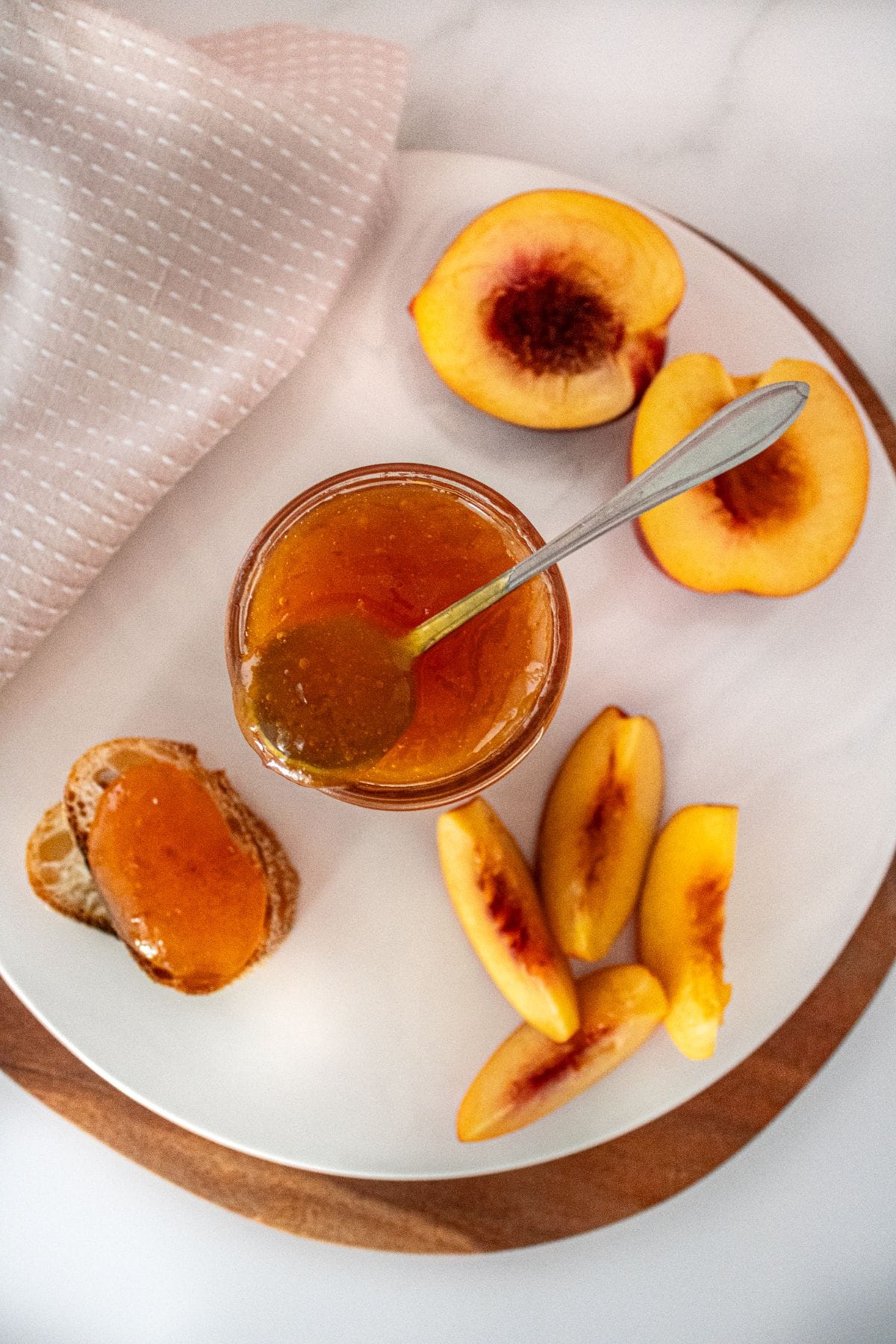 Open jar of Nectarine Jam with a spoon sitting on the jar, and some nectarine pieces around the edge.