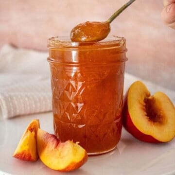 Open jar of Nectarine Jam with a spoon scooping up some jam, and some nectarine pieces around the edge.