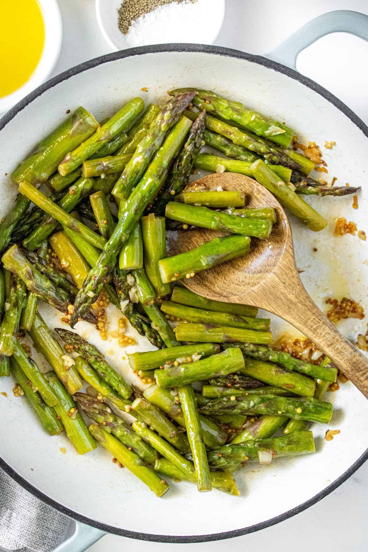 Large frying pan with Sautéed Asparagus, and a wooden spoon resting in pan.
