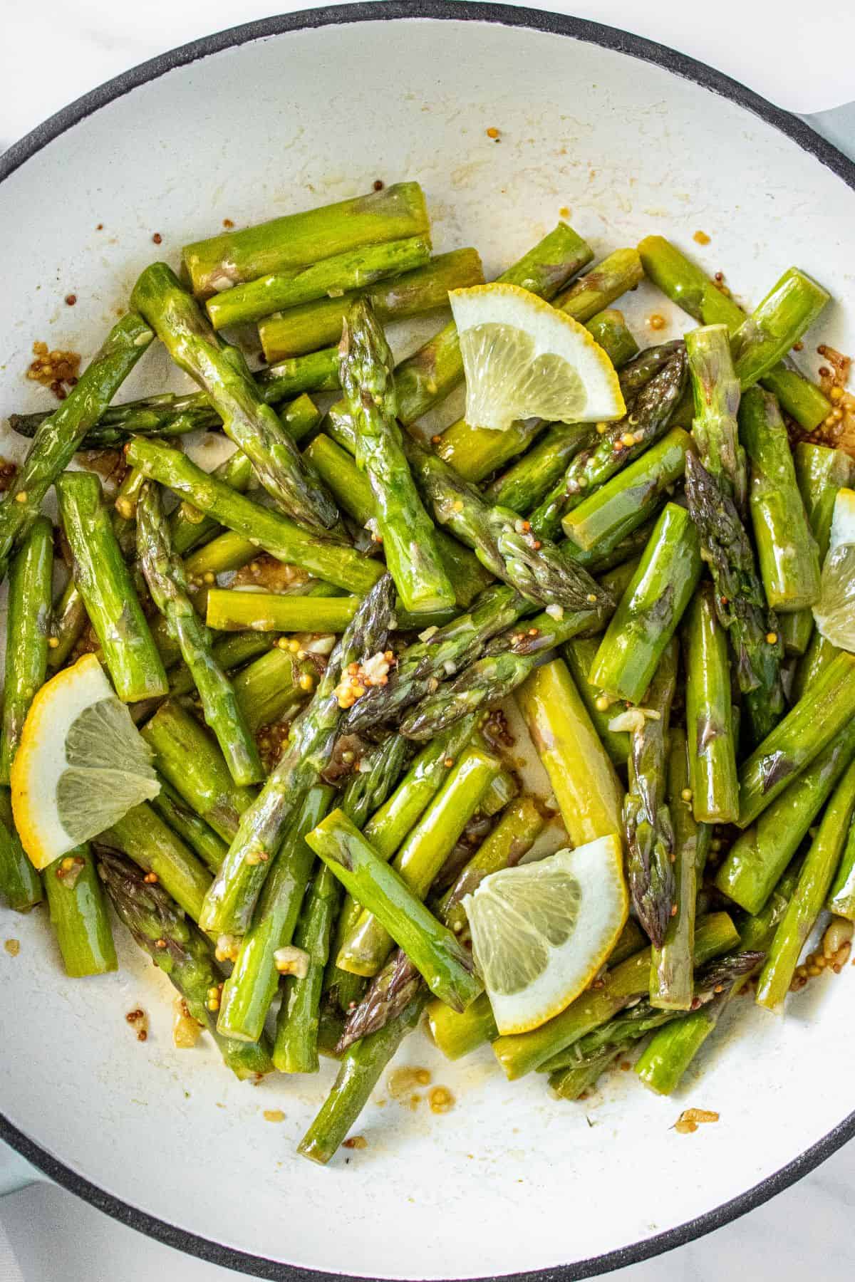 Large frying pan with Sautéed Asparagus, garnished with some slices of lemon.