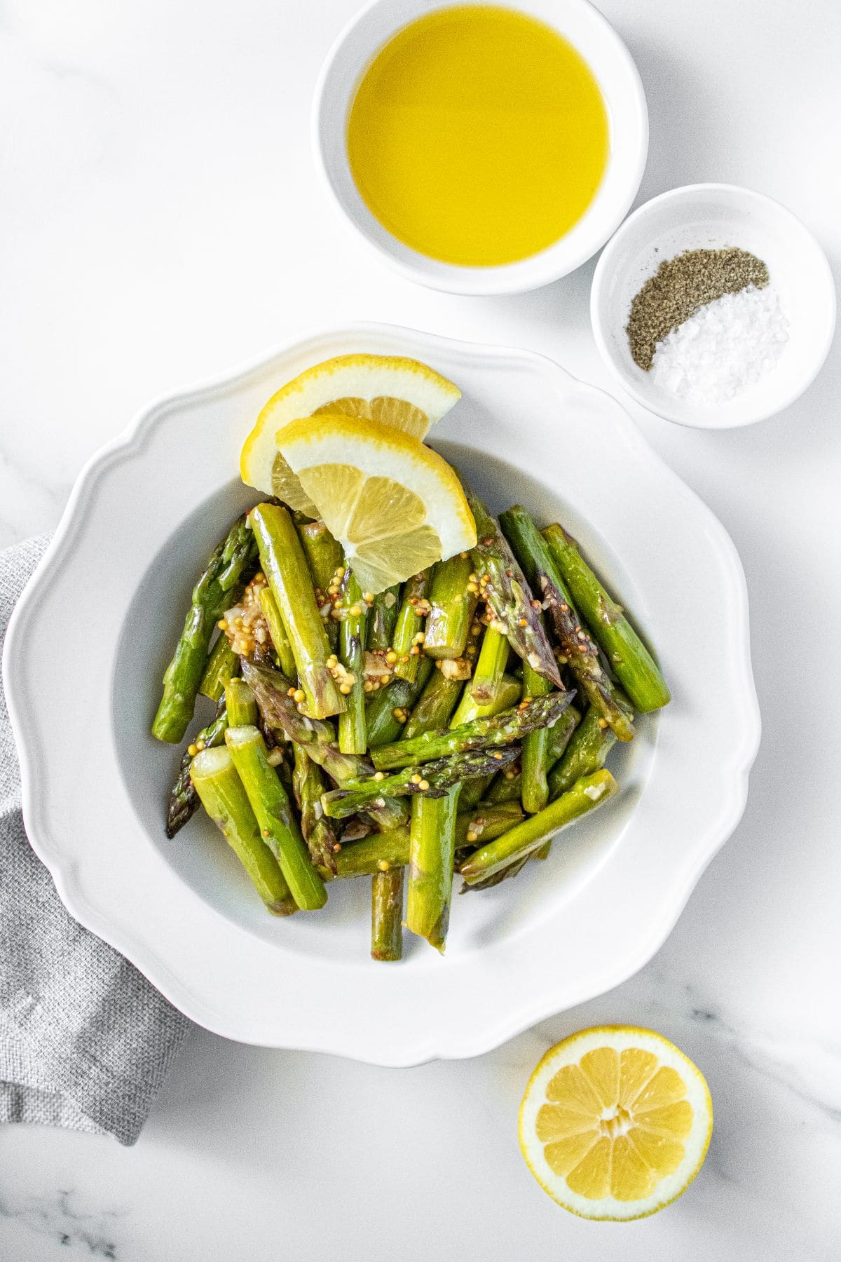 White dish with Sautéed Asparagus, garnished with some lemon slices, with some pots of seasoning around the edge.