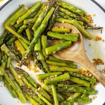 Large frying pan with Sautéed Asparagus, and a wooden spoon resting in pan.