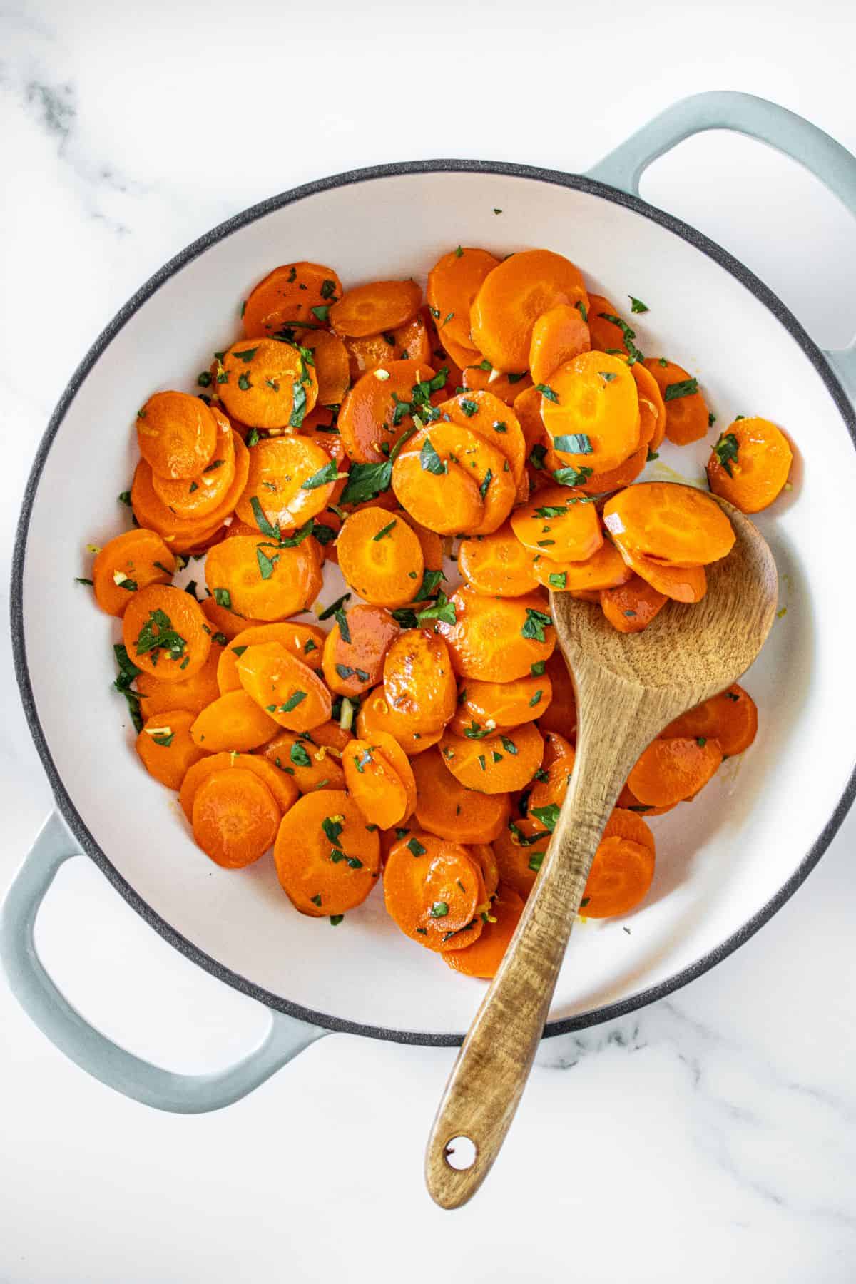Large frying pan with Sautéed Carrots, topped with gremolata, with a wooden spoon in the pan.